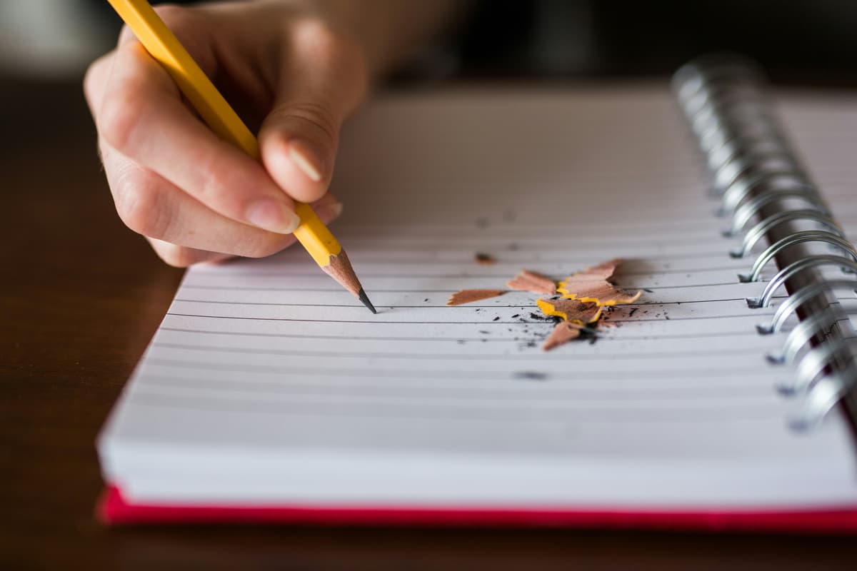 Person recording expenses in a paper ledger with a pencil